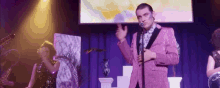 a man in a pink suit is singing into a microphone on a stage with a band .