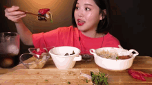 a woman in a red shirt is eating a hamburger with chopsticks