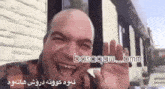a bald man is smiling and waving his hand in front of a brick wall with the words basaqaw_bmn on the bottom