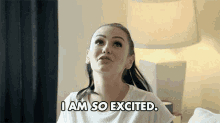 a woman is sitting on a bed and says i am so excited .