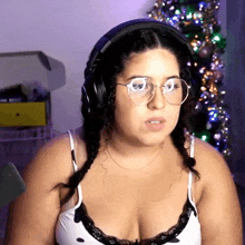 a woman wearing headphones and braids looks at the camera in front of a christmas tree
