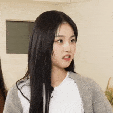 a woman with long black hair is wearing a white shirt and a grey sweater