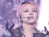 a woman with pink hair is wearing a microphone and gloves and the word team is on the bottom right