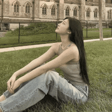 a woman in a tank top and jeans is sitting in the grass