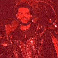 a man with a beard is wearing a red jacket and standing in front of a red background .