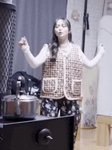 a woman in a vest is standing in front of a kettle .