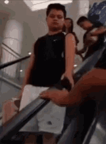 a man in a black nike tank top is standing on an escalator