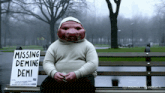 a man sitting on a park bench with a sign that says missing deming demi
