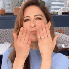 a woman is blowing a kiss with her hands while wearing a ring on her finger .