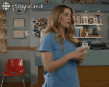 a woman in scrubs is dancing in front of a sign that says schittscreek