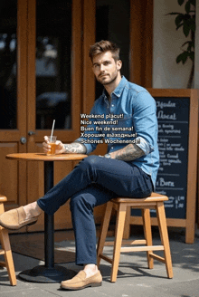 a man in a denim shirt sits at a table with a drink
