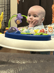 a baby sitting in a blue and white walker with a purple monkey on it