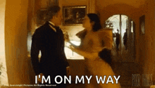a man in a tuxedo and a woman in a dress are dancing in a living room .