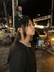 a girl wearing a black beanie stands in front of a sign that says ' estrada '