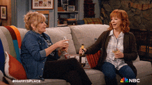 two women are sitting on a couch holding wine glasses and a bottle of wine with a nbc logo in the corner
