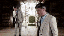 two men in suits are standing in a room with a green chair