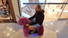 a man is riding a pink unicorn in a mall