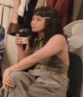 a woman is sitting in a chair holding a cup of coffee and a fan .