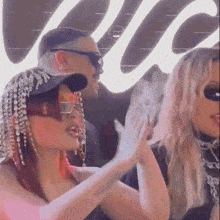 a woman wearing sunglasses and a hat with rhinestones on it is giving a high five to another woman