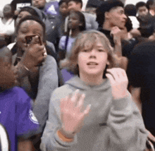 a boy is standing in a crowd of people waving his hand .