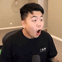 a man is sitting in front of a microphone with his mouth open and making a surprised face .