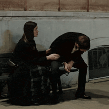 a man and a woman sit on a bench and the woman is touching the man 's arm