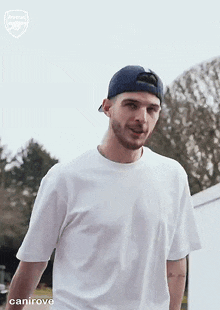 a man wearing a white t-shirt and a blue baseball cap is standing in a field .
