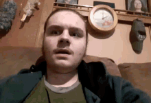 a man sitting on a couch in front of a clock and a hat that says psu on it