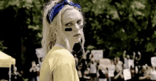 a woman wearing a bandana and a yellow shirt is standing in front of a crowd of people at a protest .