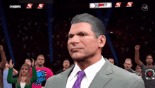 a man in a suit and tie stands in front of a crowd watching a wrestling match on wwe hd