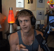 a man wearing headphones and a tank top stands in front of a microphone and a lava lamp