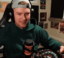 a man wearing headphones and a green hoodie is sitting in front of a microphone and smiling .