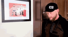 a man wearing a black hat is standing in front of a framed picture of wrestlers .
