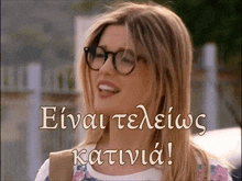a woman wearing glasses is smiling with the words " einai teleios katinia " written below her