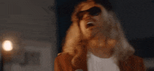 a man with long blonde hair is singing into a microphone while wearing sunglasses .