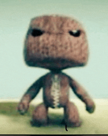 a brown stuffed animal with a black eye is standing on a sandy surface