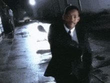 a man in a suit and tie is walking down a sidewalk at night .