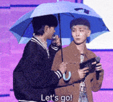 a man holding an umbrella stands next to another man holding a microphone and says let 's go