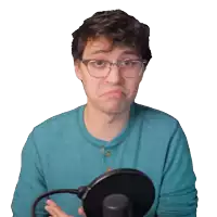 a man wearing glasses and a blue shirt is holding a microphone and making a sad face