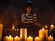 a woman in a black and white striped shirt sits in front of candles