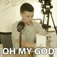 a man is sitting in front of a microphone with the words `` oh my god '' written on it .