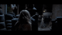 a woman is standing in a dark room looking out a window at a man .