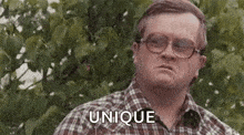a man in a plaid shirt and glasses is standing in front of a tree .