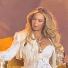 a woman in a white dress with fringe on the sleeves is singing into a microphone
