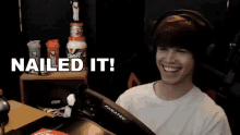 a man wearing headphones is sitting in front of a steering wheel with the words nailed it written above him .