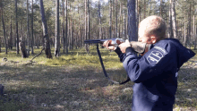 a boy is holding a shotgun in the woods and has a patch on his jacket that says ' army ' on it