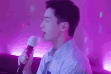 a man is singing into a microphone in a room with purple lights behind him .