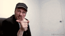 a man wearing glasses and a hat is pointing at the camera with gifrun.com written on the bottom right