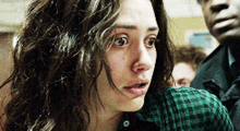 a woman with curly hair is wearing a plaid shirt and looking at something .