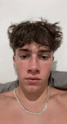 a shirtless young man wearing a silver chain around his neck is making a sad face .